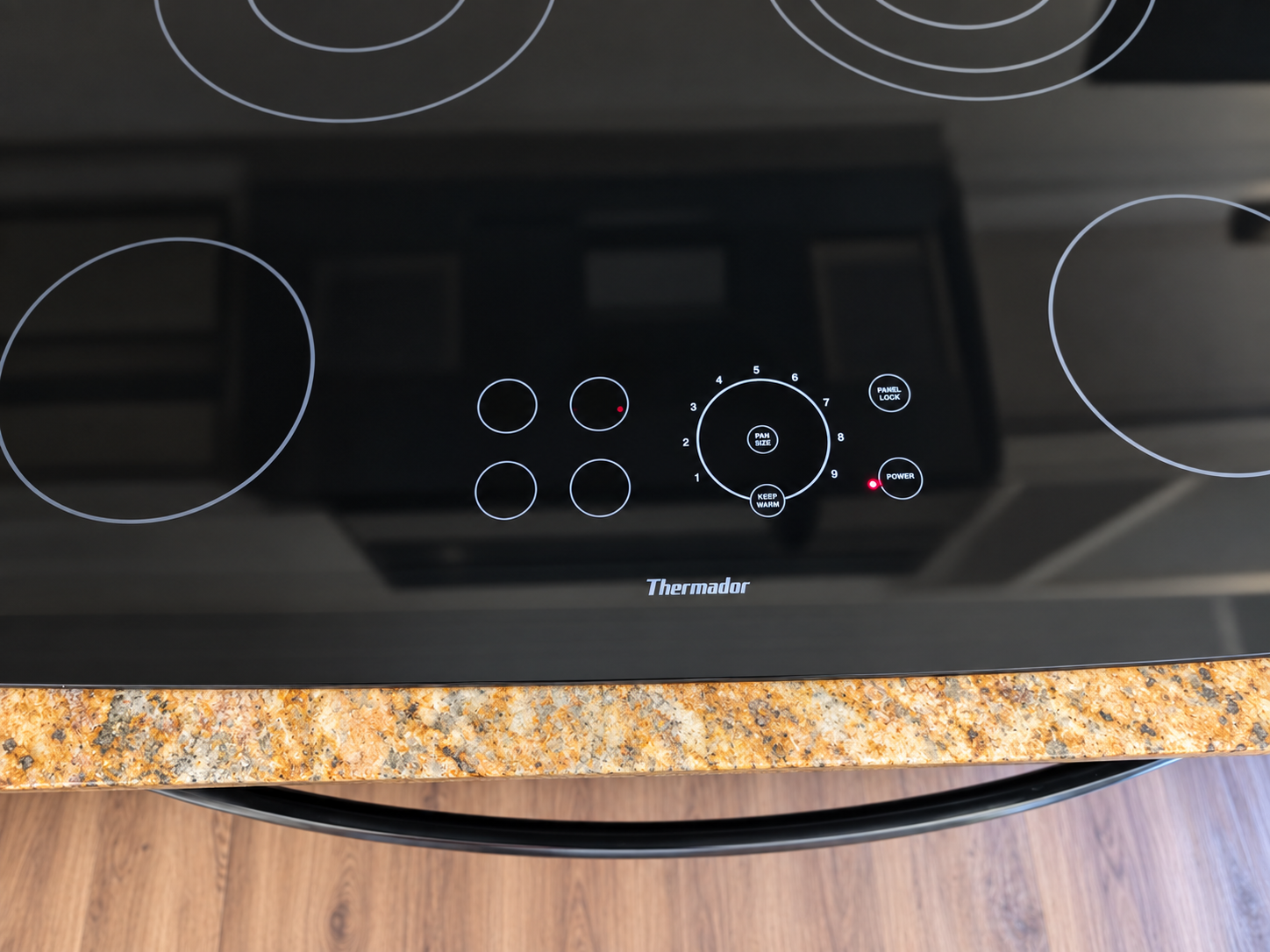 Thermador glass cooktop showing four burner-selection circles, the numbered heat control, PAN SIZE, PANEL LOCK, and POWER.
